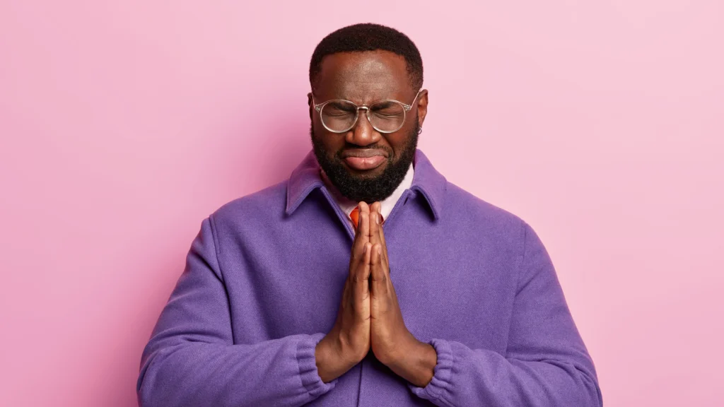 hopeful black man keeps both hands pressed together praying gesture believes good luck scaled and improve his mood